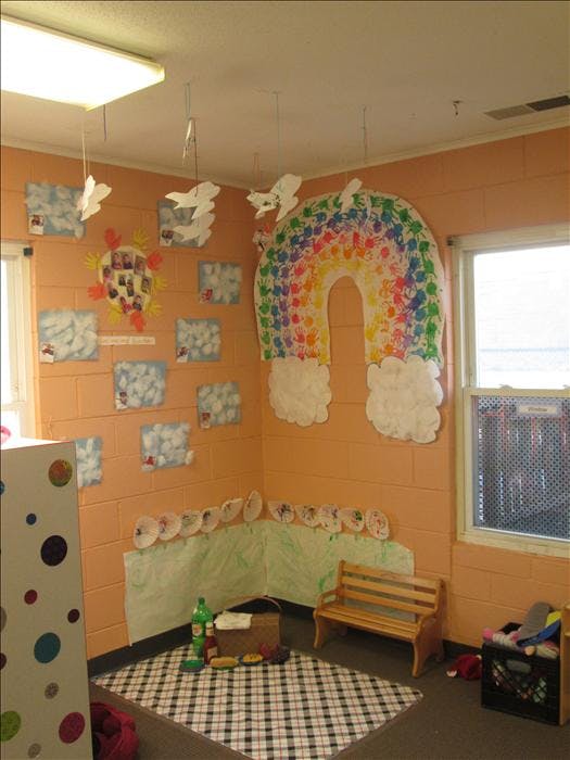 Classroom corner with rainbow handprint art, paper planes, and a picnic setup