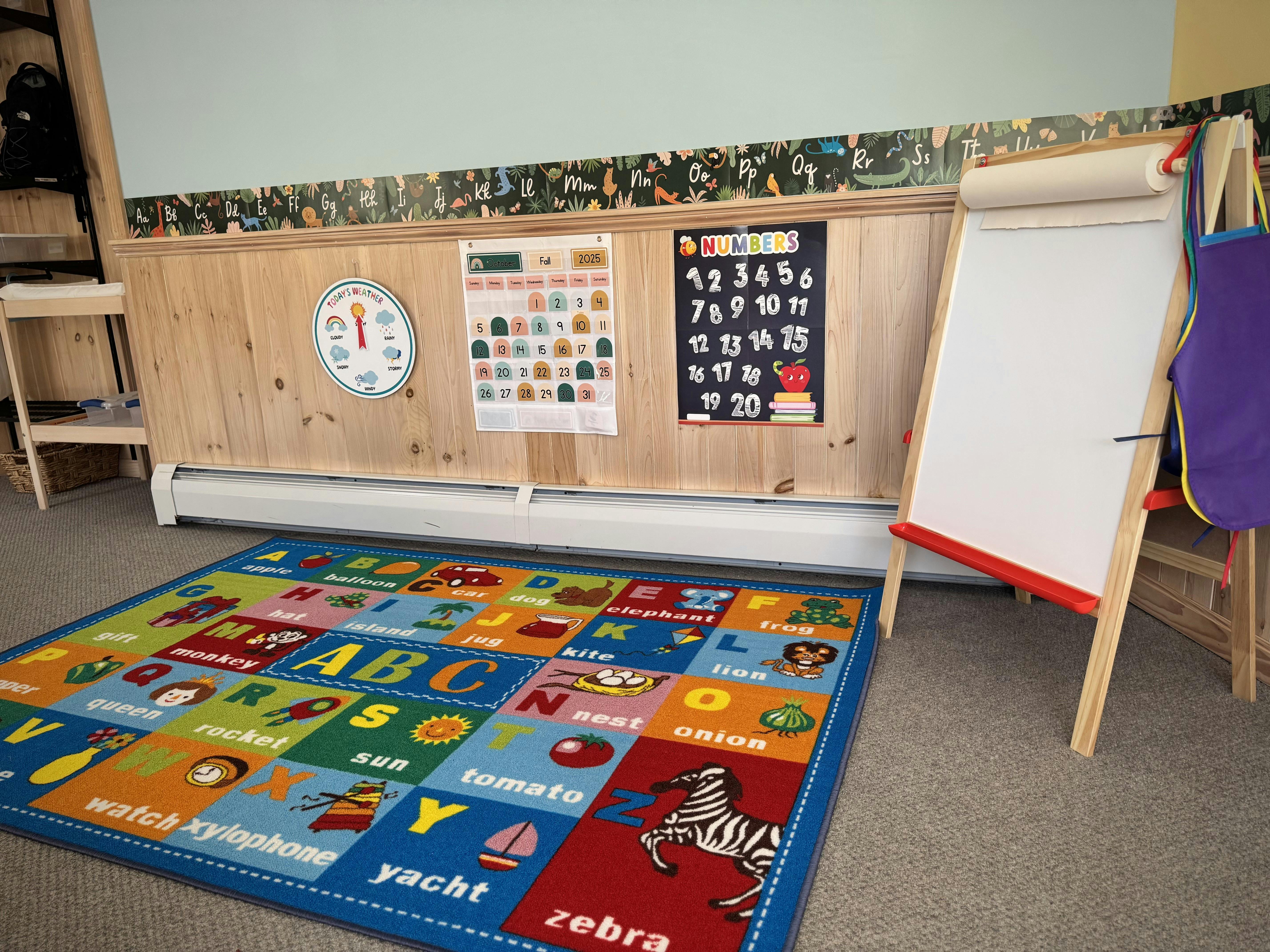 Alphabet rug on floor in a classroom with easel and wall decorations