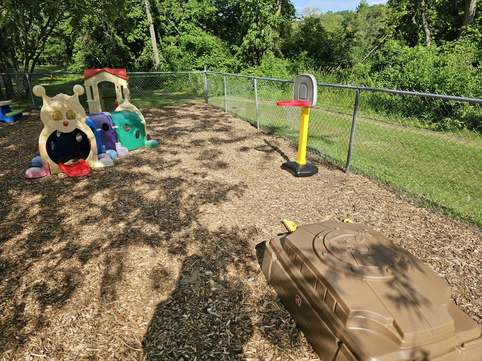 Playground equipment including a plastic tunnel, basketball hoop, and sandbox