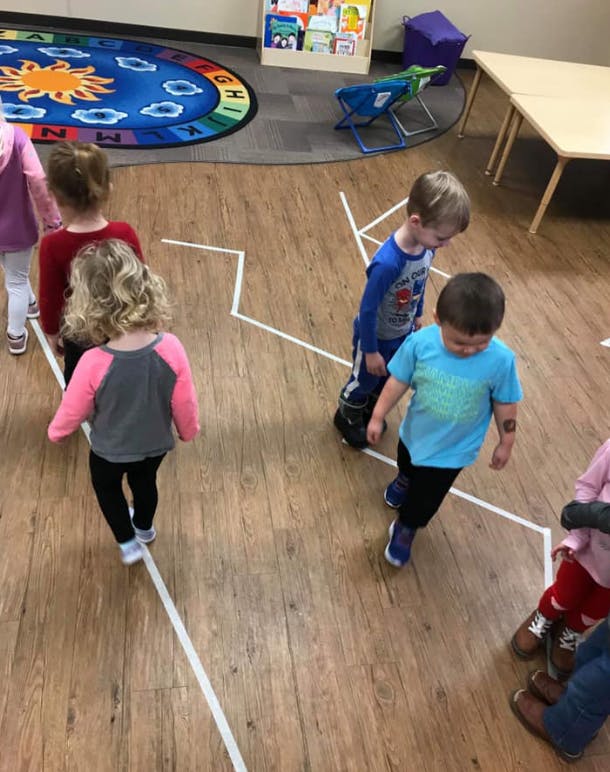 Children walking on white lines on a wooden floor in a classroom