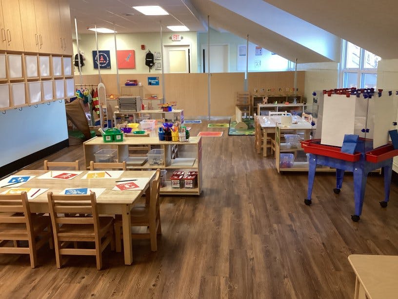 Empty classroom with small tables and chairs, shelves, and play areas