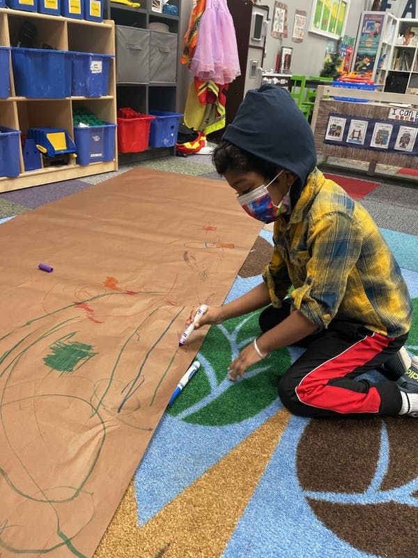 Child in a mask drawing on a large piece of paper on the floor