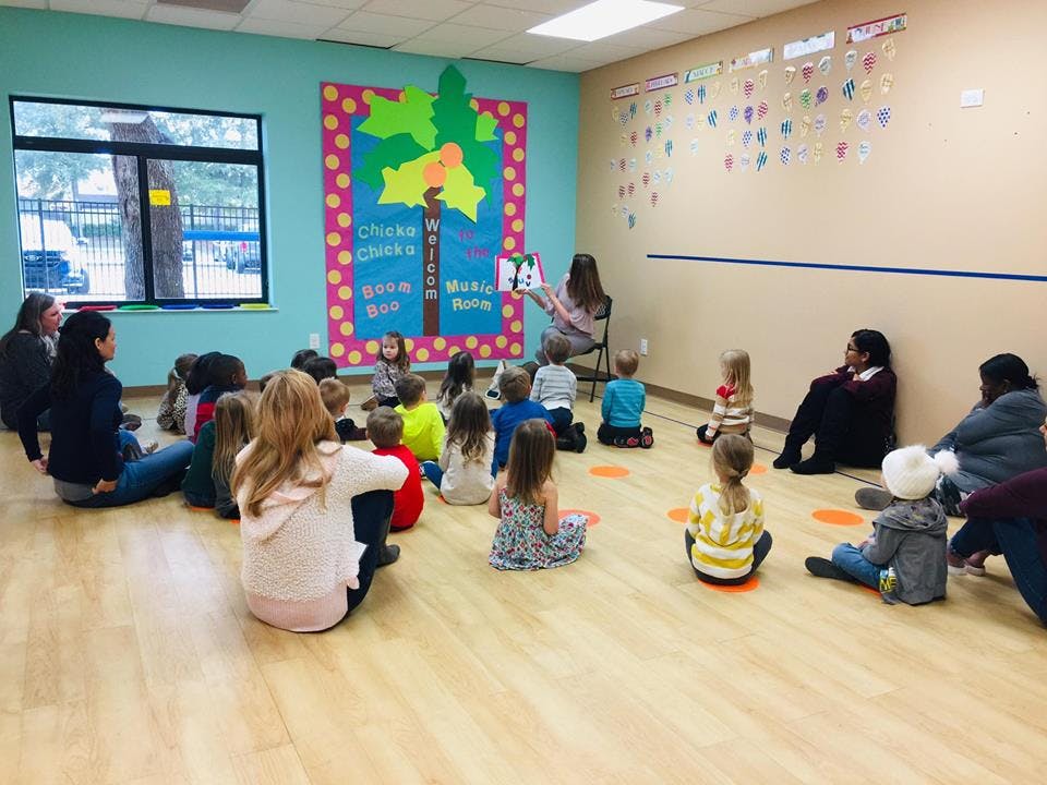 Adult reading a book to a group of children and adults sitting on the floor