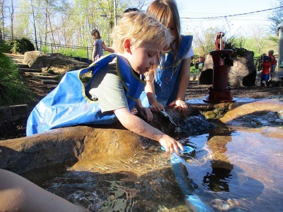 Child playing in water with a toy boat, another child nearby