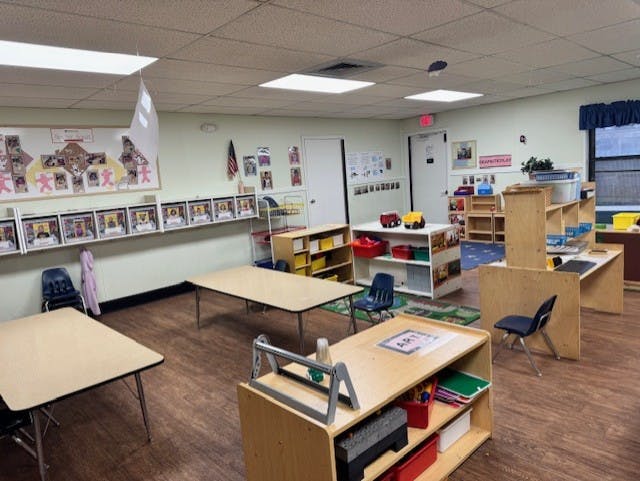 Empty classroom with small tables, chairs, and shelves with toys