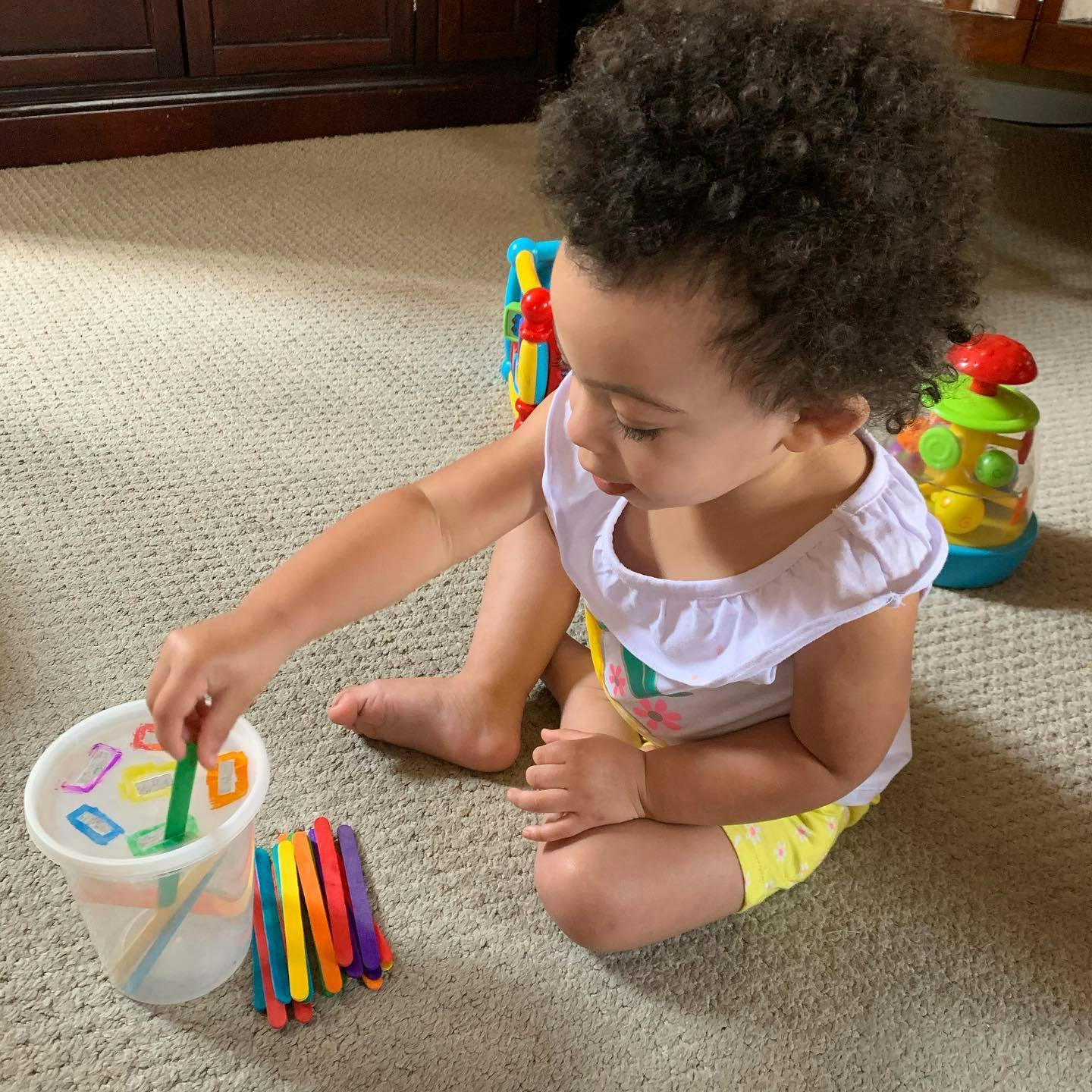 Child playing with colorful sticks and a clear cup