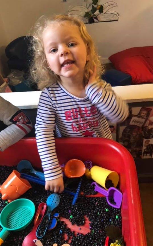 Child playing in a red bin with black sensory filler and colorful toys