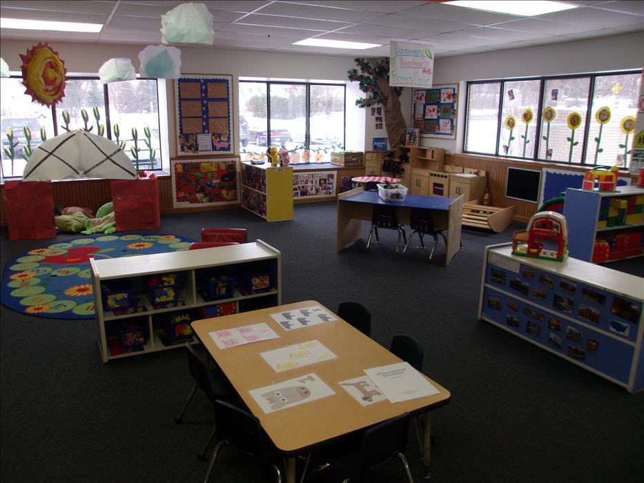 A colorful empty classroom with various play areas and small tables with chairs