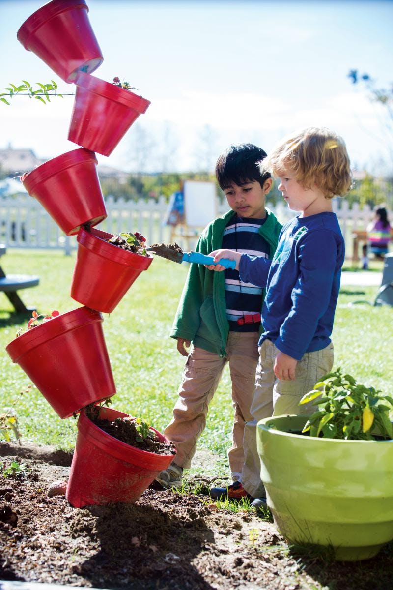 Two children planting in a garden with stacked red pots