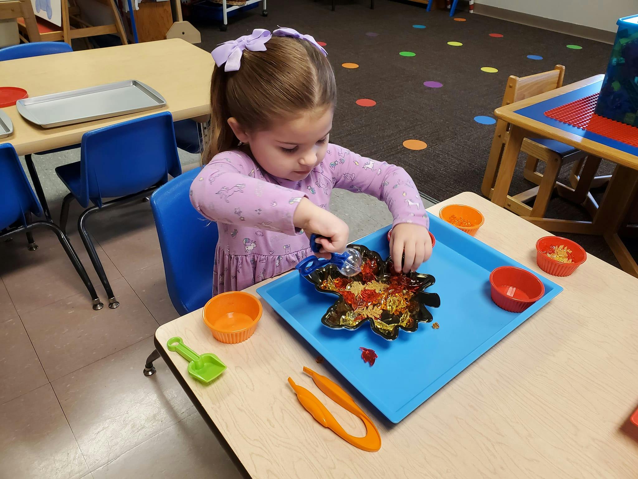 Child playing with sensory bin materials at a table in a classroom