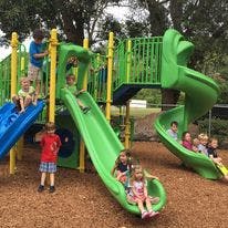 Children playing on a green and blue playground slide structure with slides