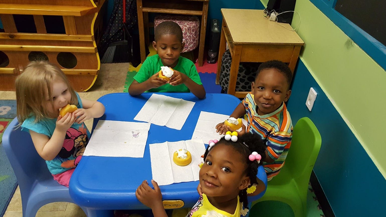 Four children sitting at a table eating donuts