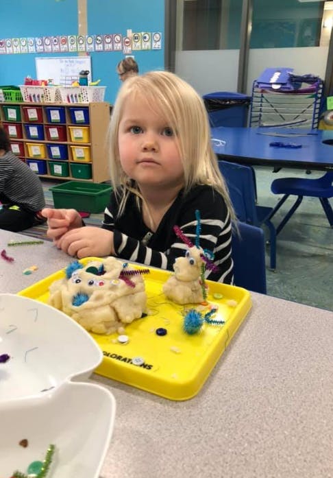 Child at a table with playdough creations on a yellow tray