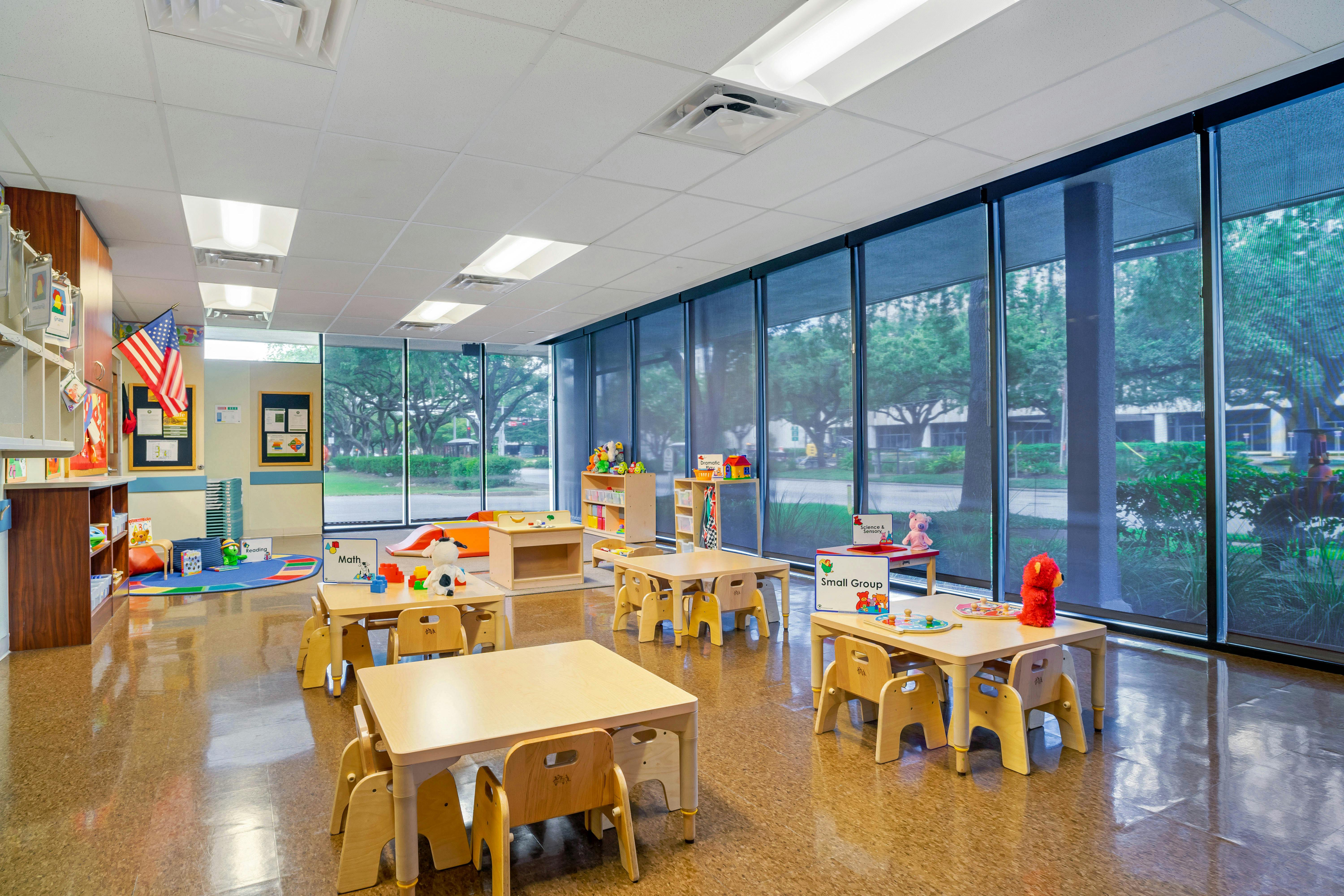 Empty classroom with small tables and chairs, toys, and large windows