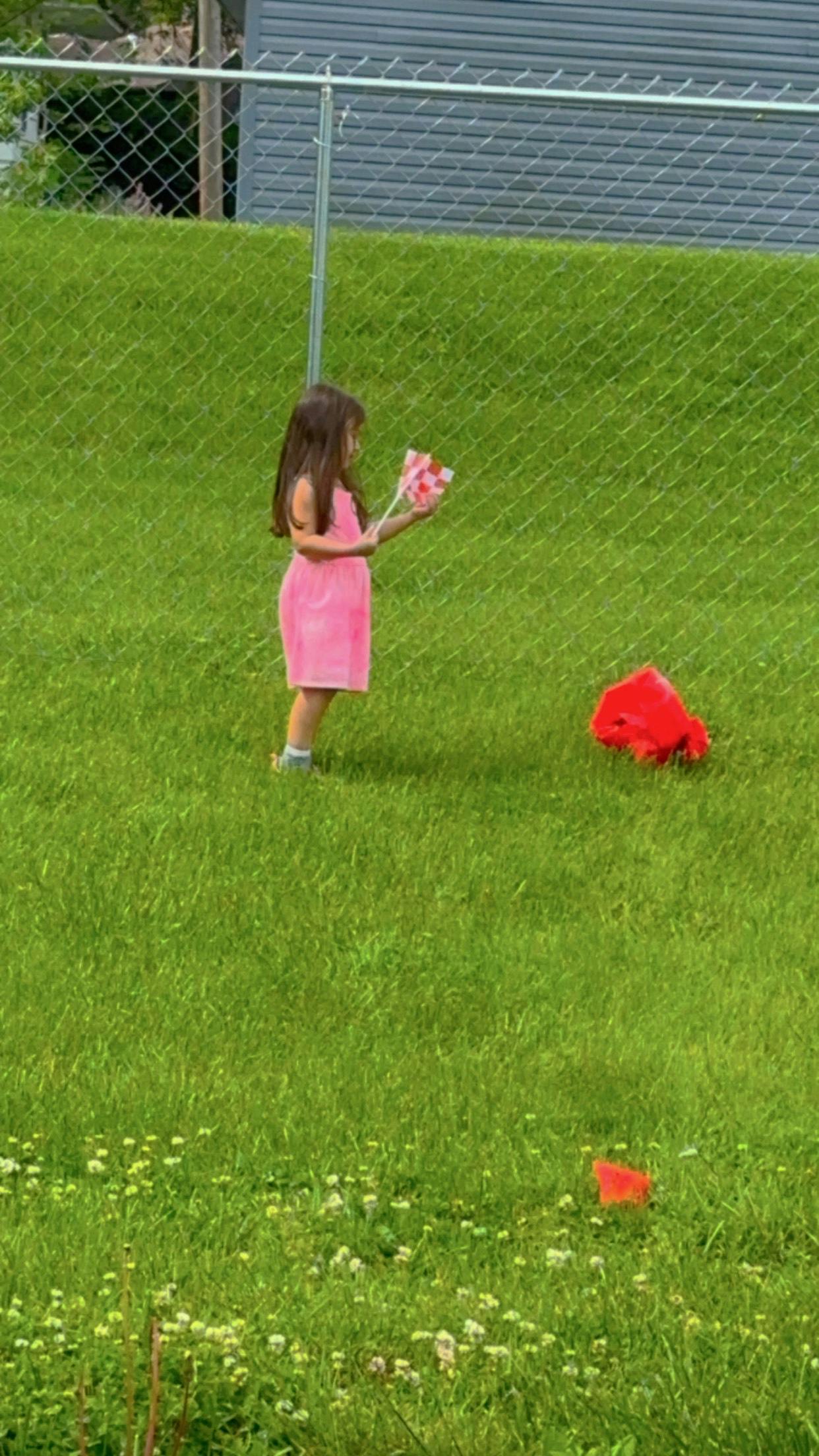 Child in a pink dress holding a pinwheel in a grassy area