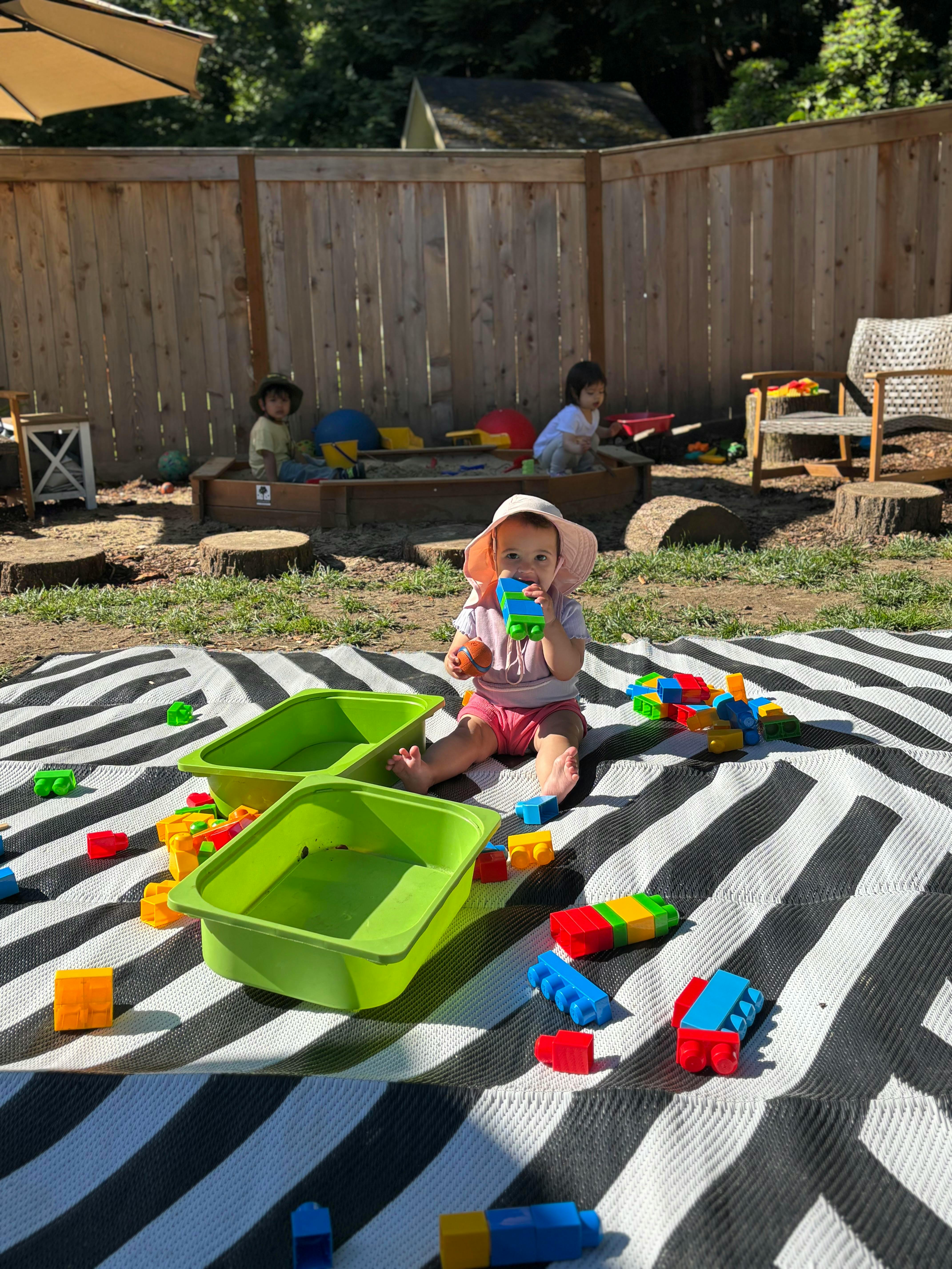 Child wearing a sun hat sitting on a striped mat playing with building blocks