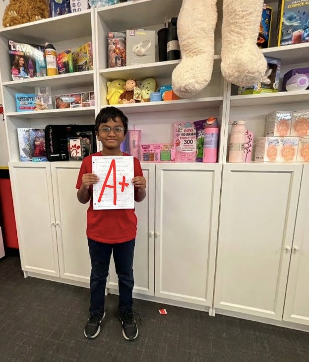 Child in glasses holding up a paper with a large red A+