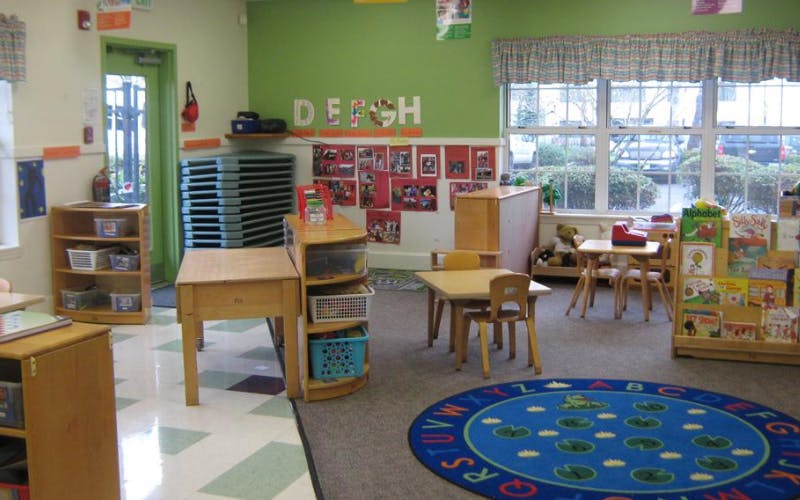 A classroom with small tables, chairs, and a round rug