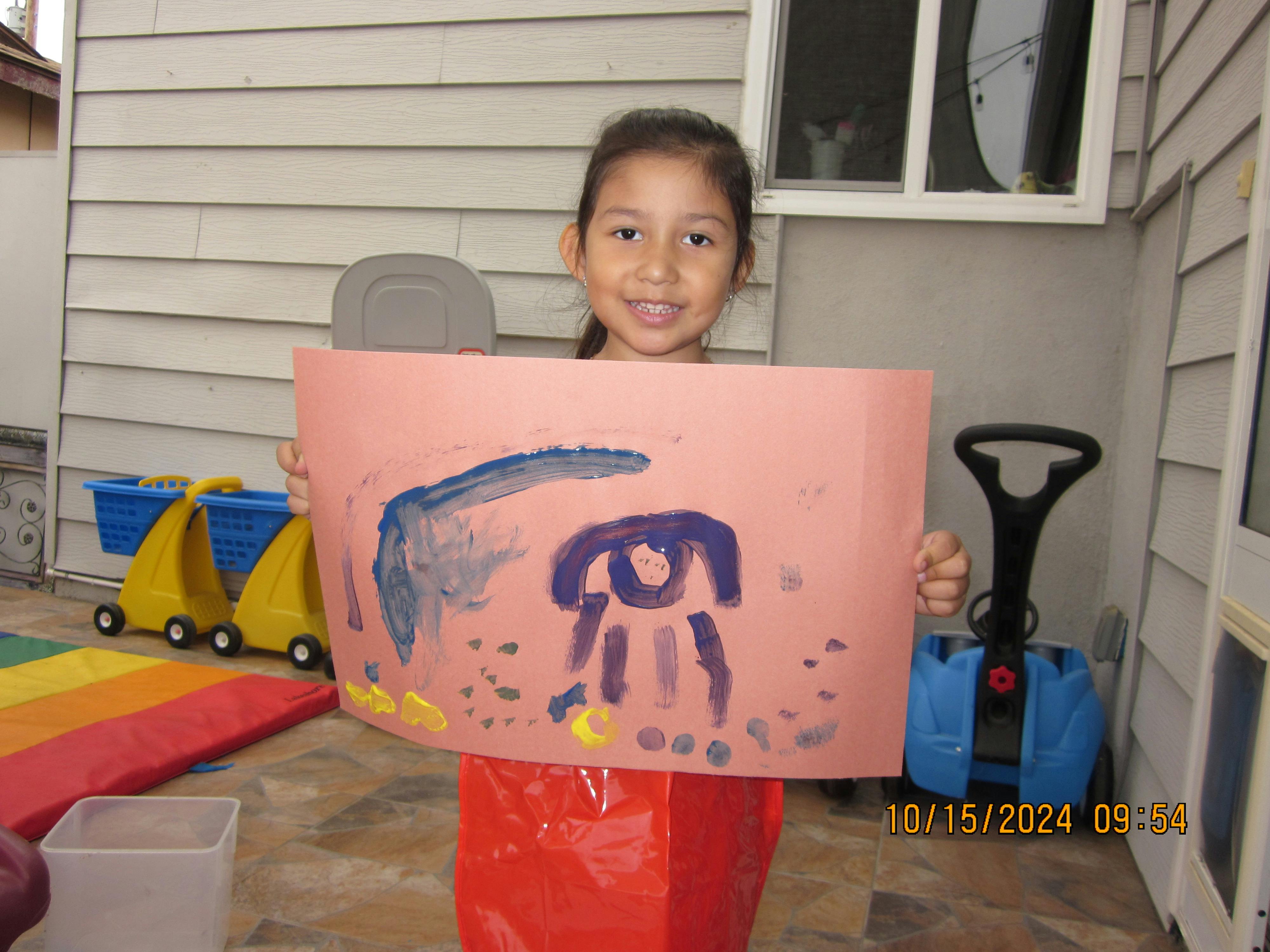 Child holding up a painting on a pink sheet of paper