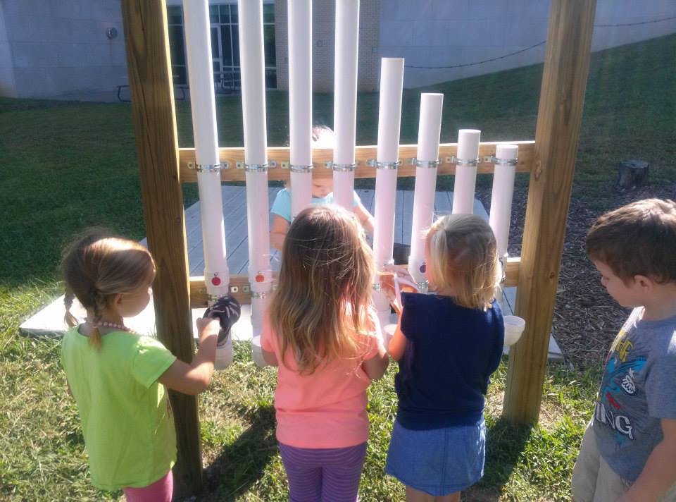 Children playing with a PVC pipe musical instrument outdoors