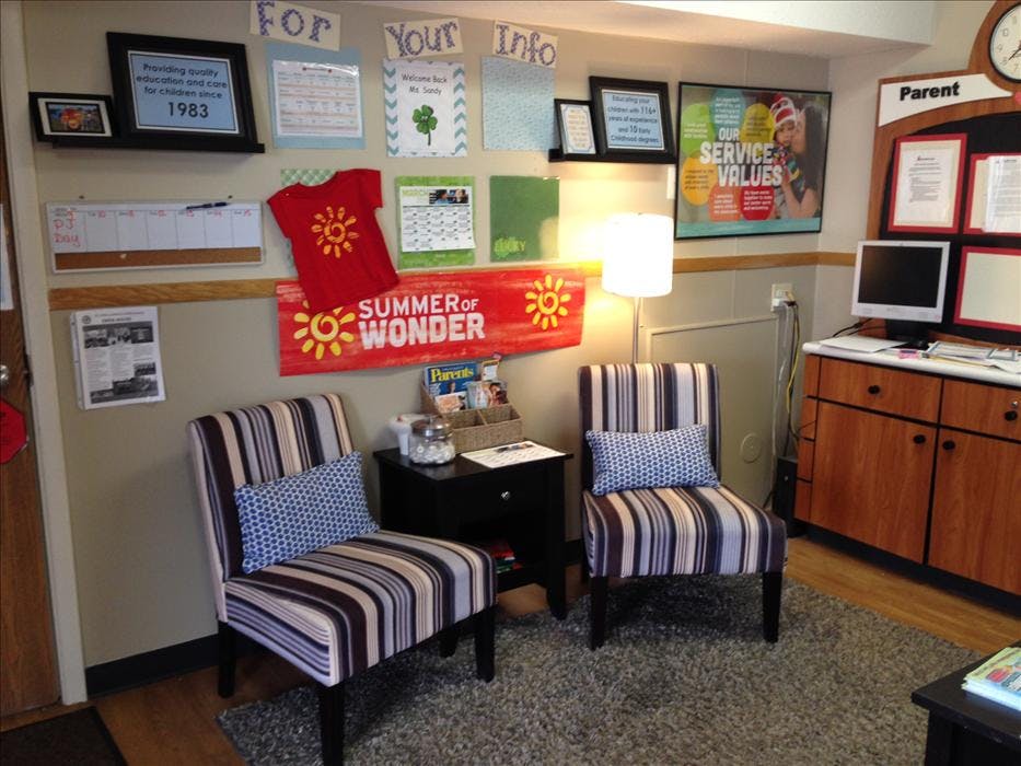 A waiting room with two striped chairs, a small table, a lamp, and informational posters