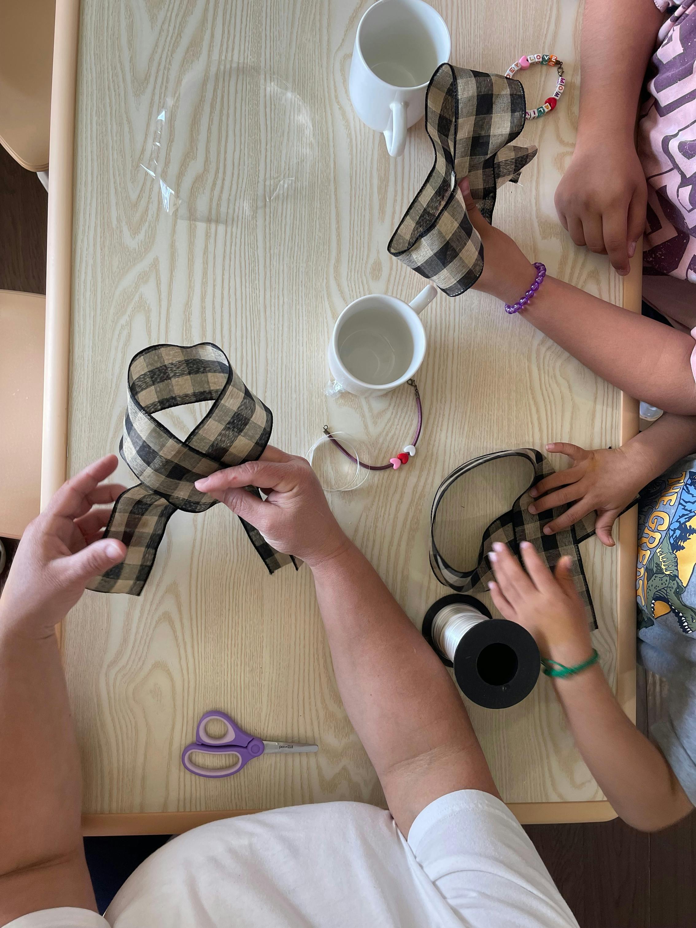 People crafting bows from plaid ribbon on a table