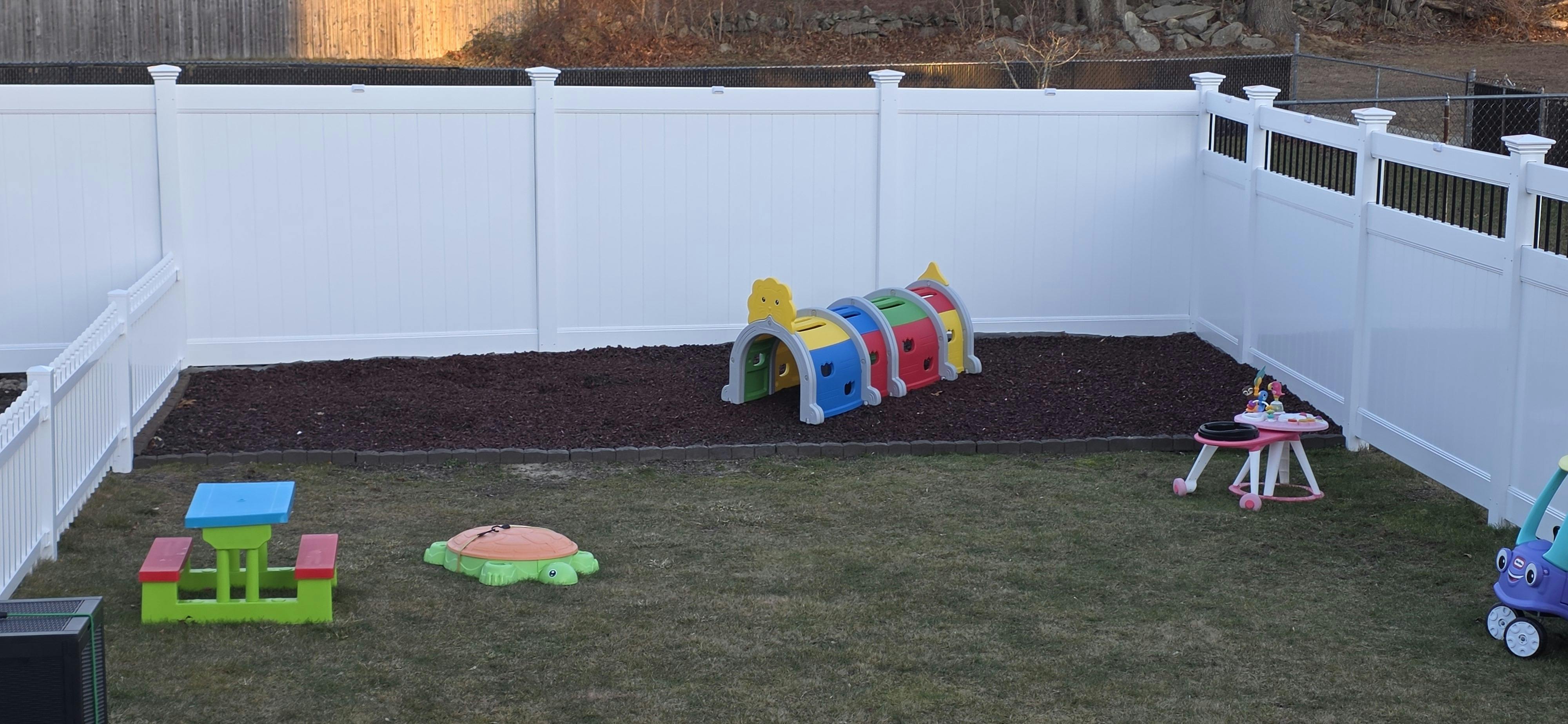 backyard with white fence, colored play tunnel, turtle sandbox, and play picnic table