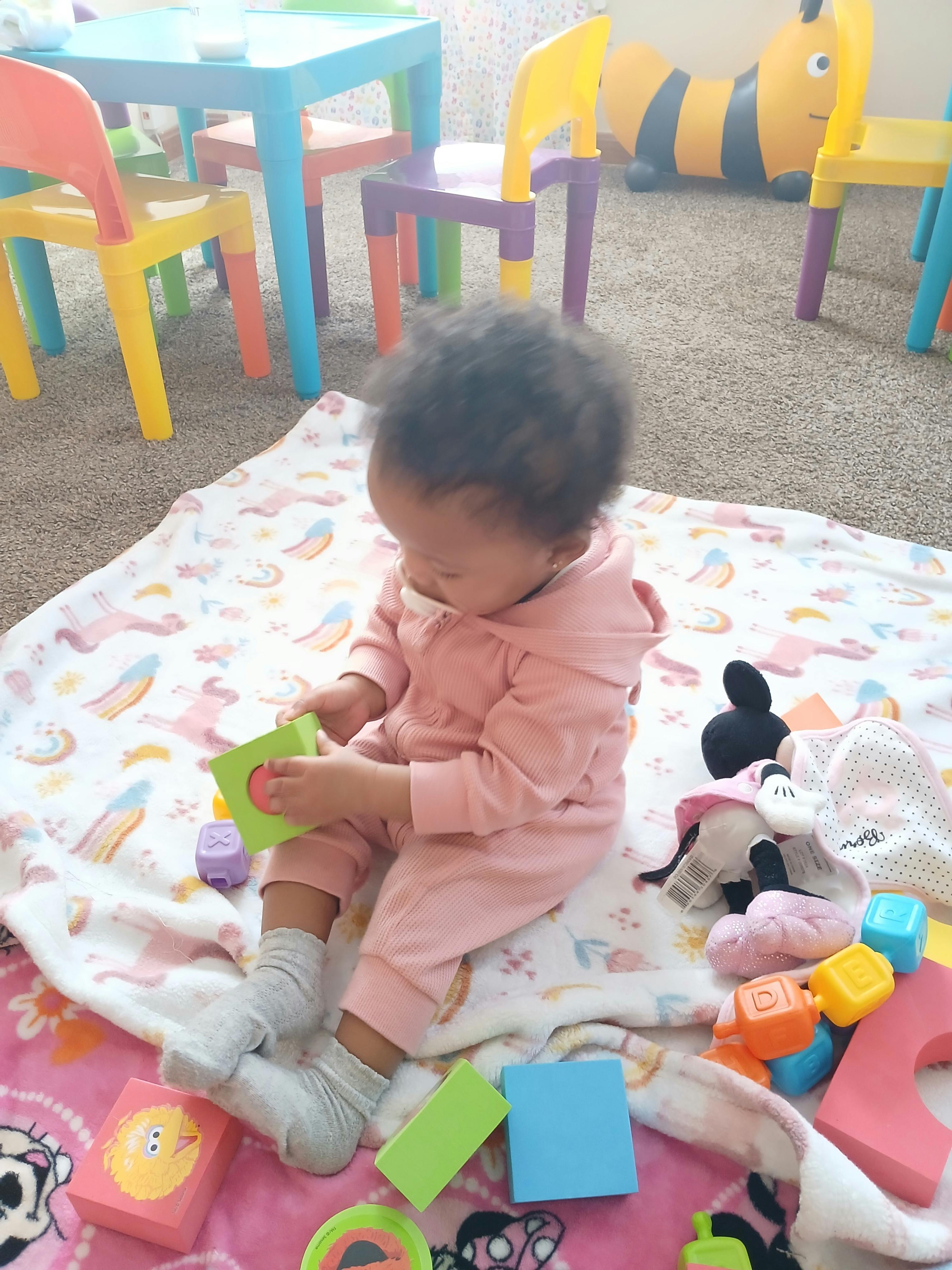 Child in pink playing with a green toy on a blanket