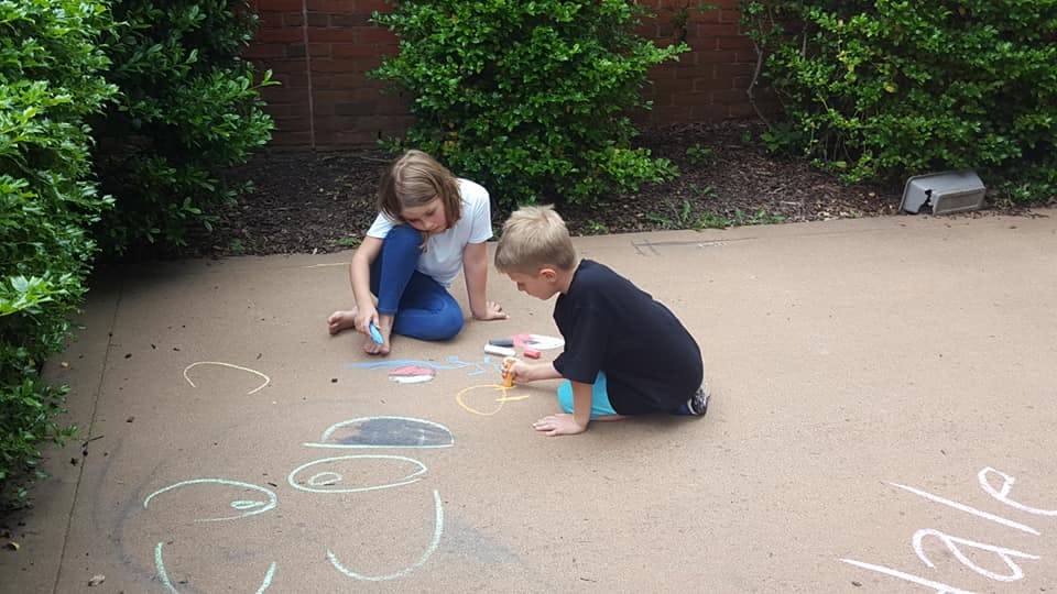 Two children drawing with chalk on pavement