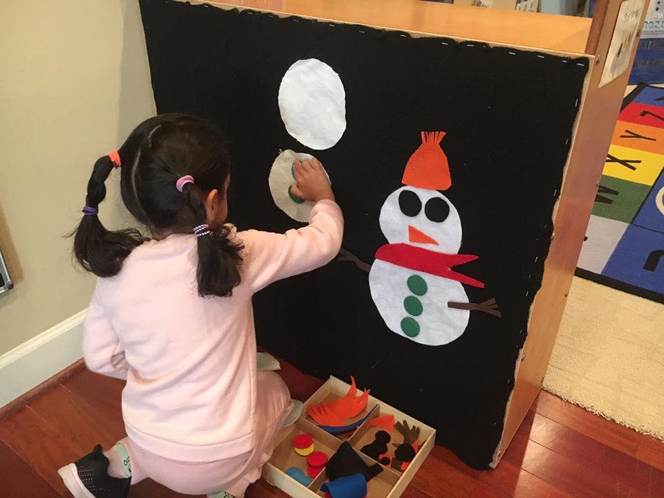Child placing a white circle on a black board next to a snowman cutout
