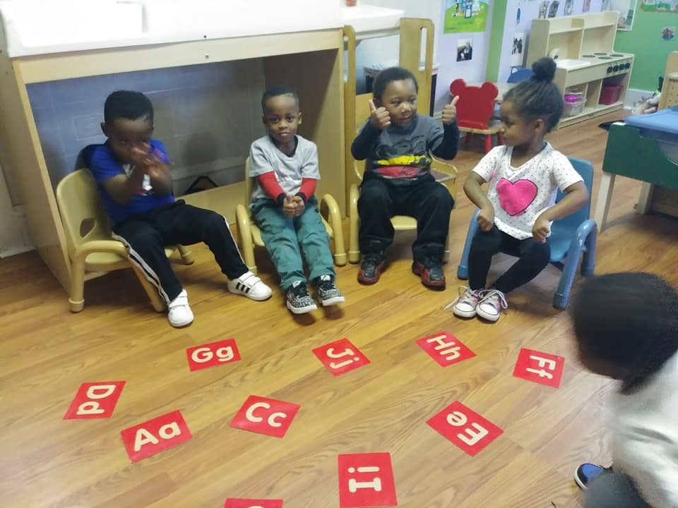 Children sitting on chairs in a classroom with alphabet letters on the floor