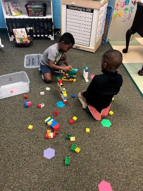 Two children playing with building blocks on a carpeted floor