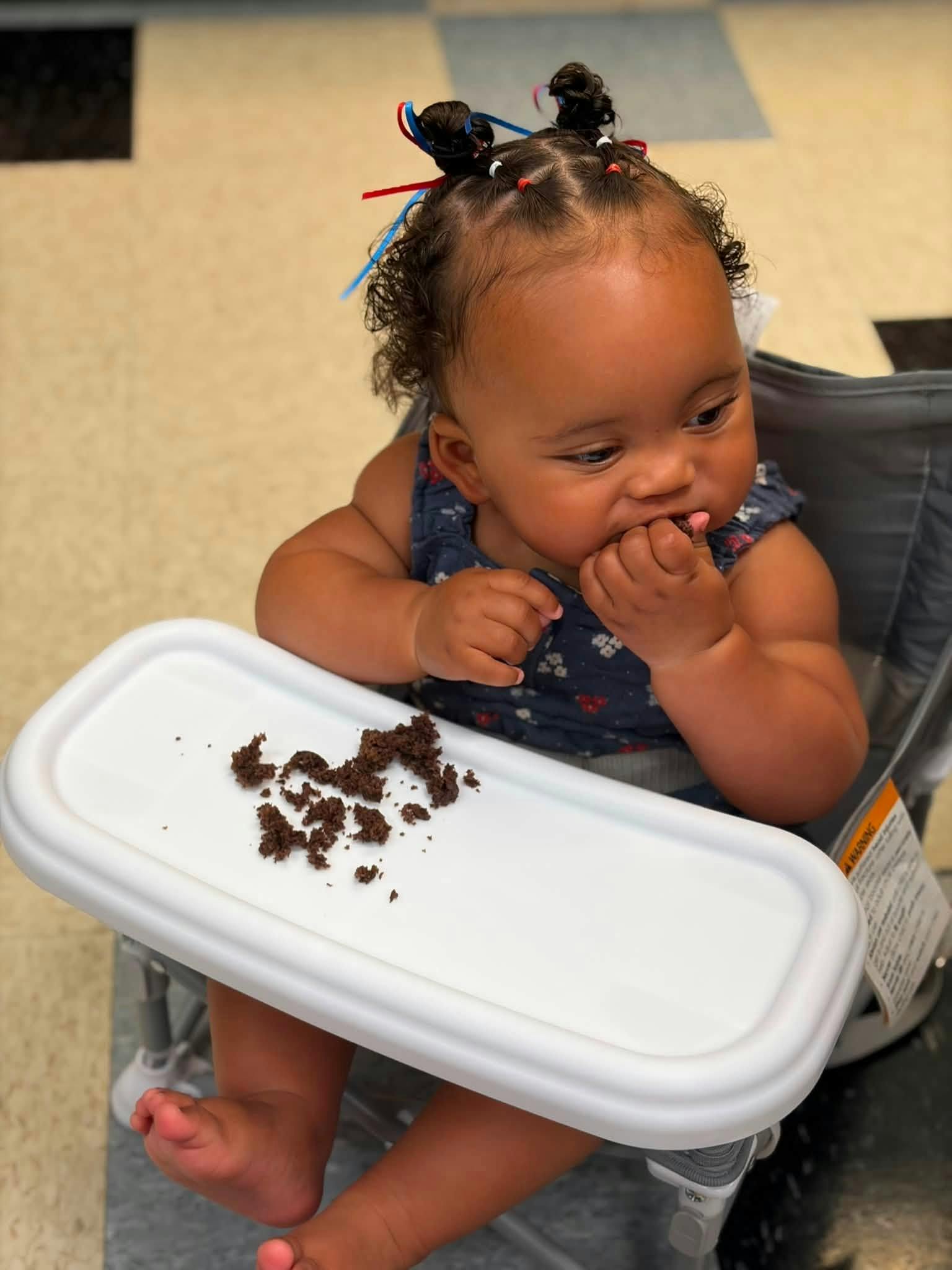 Child sitting in a high chair eating cake pieces