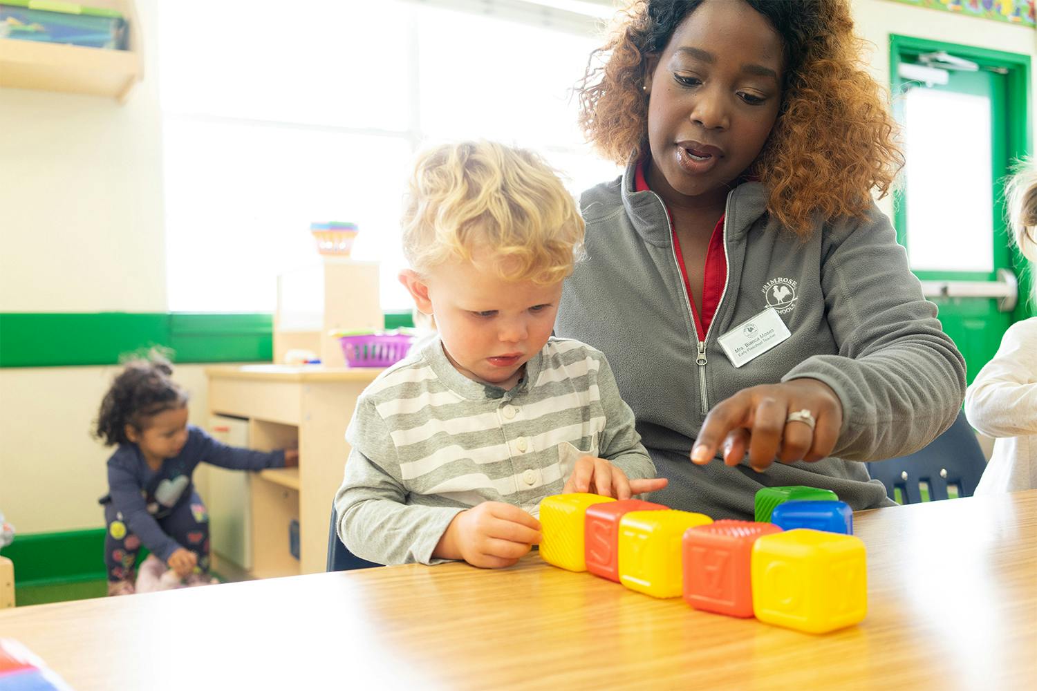 Adult and child playing with colorful blocks on a table in a classroom