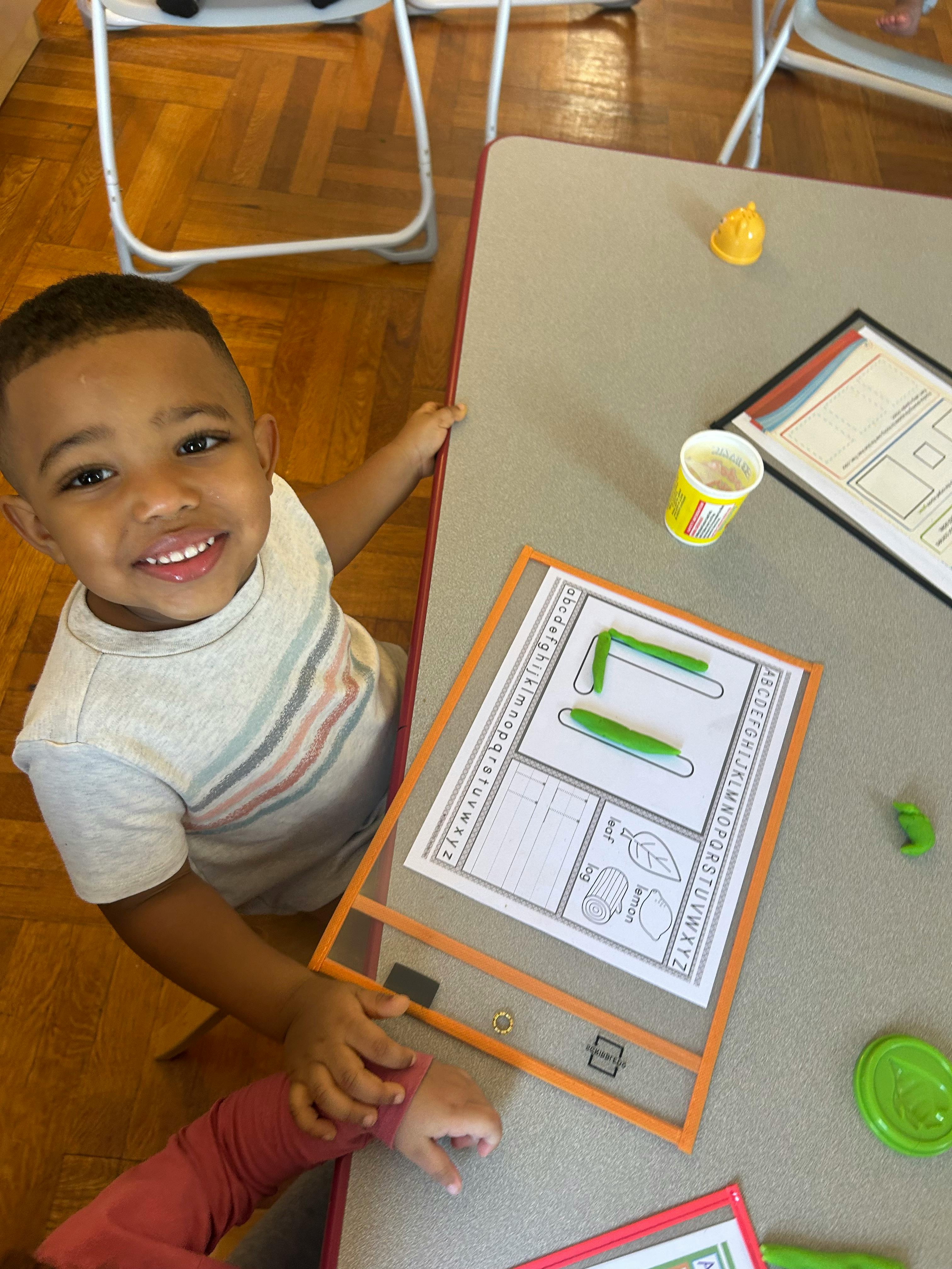 Child smiling at a table with a worksheet