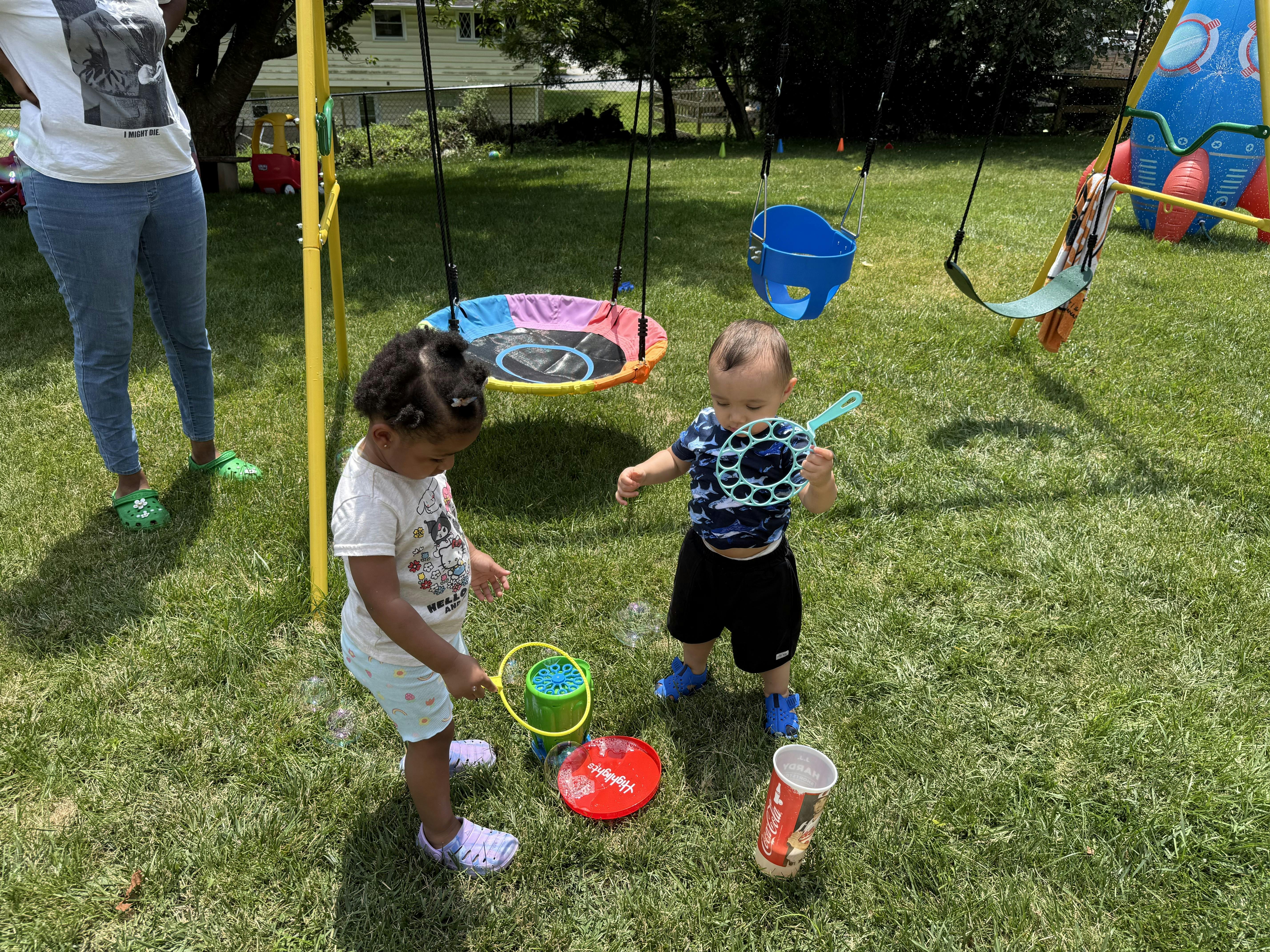 Two children playing with bubble wands in a grassy yard