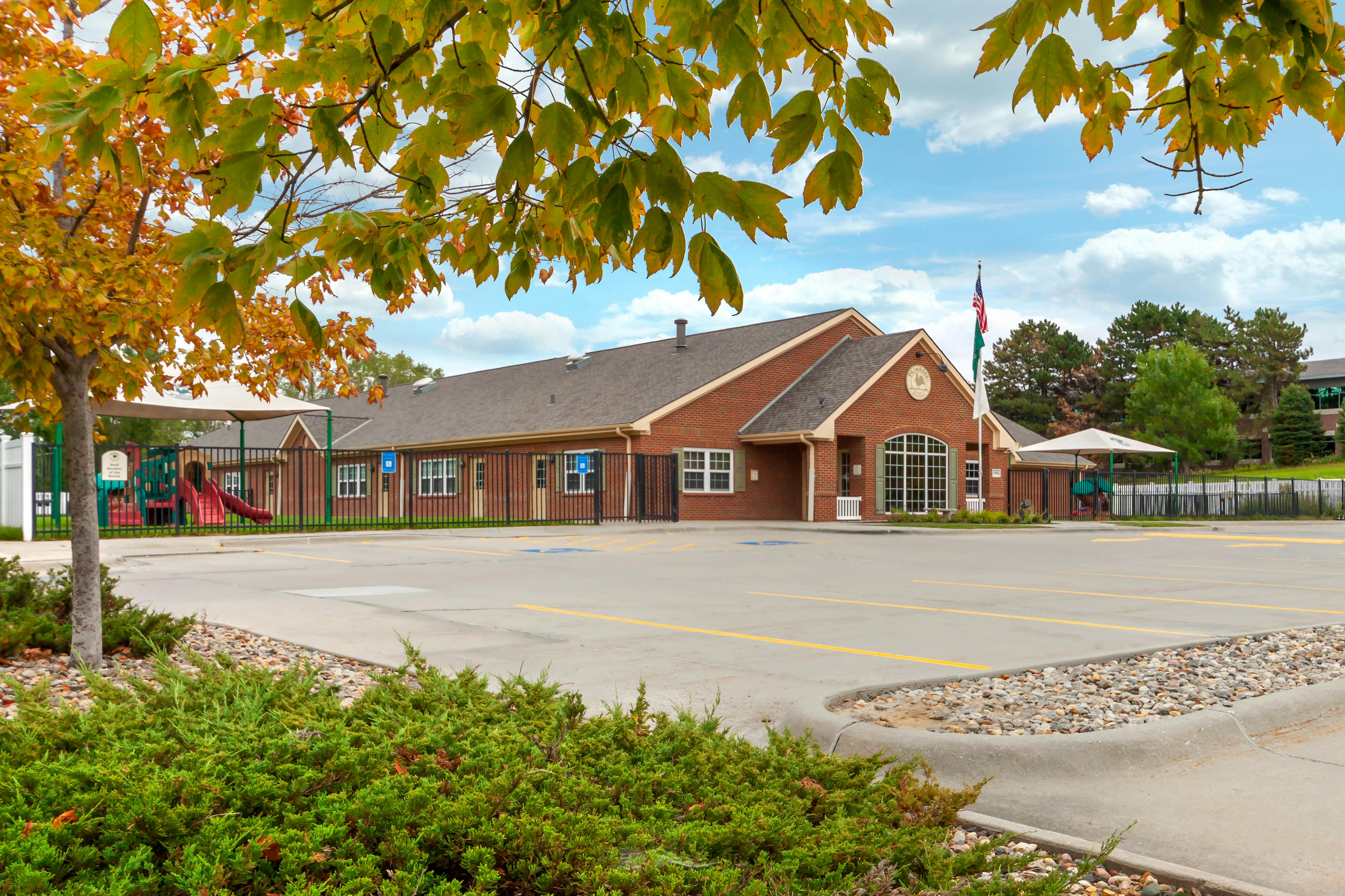 Building with a parking lot and playground in front, partially obscured by trees