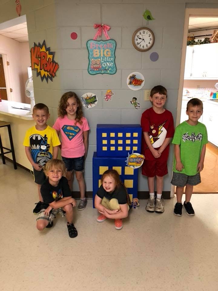 Six children posing in a room with superhero decorations