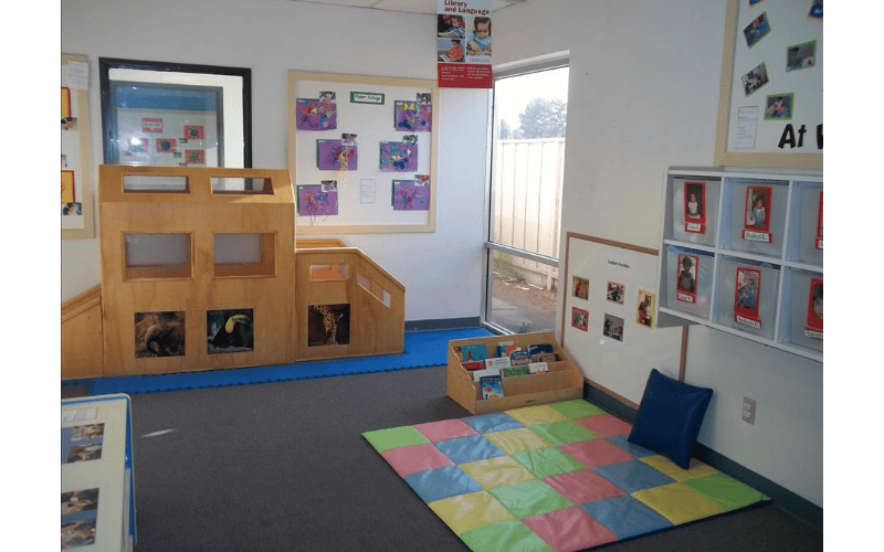 Classroom with child-sized wooden play structure, book display, and colorful floor mat