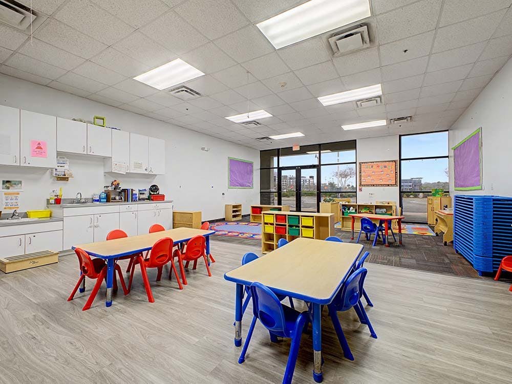 Classroom with small tables and chairs, a sink area, and large windows