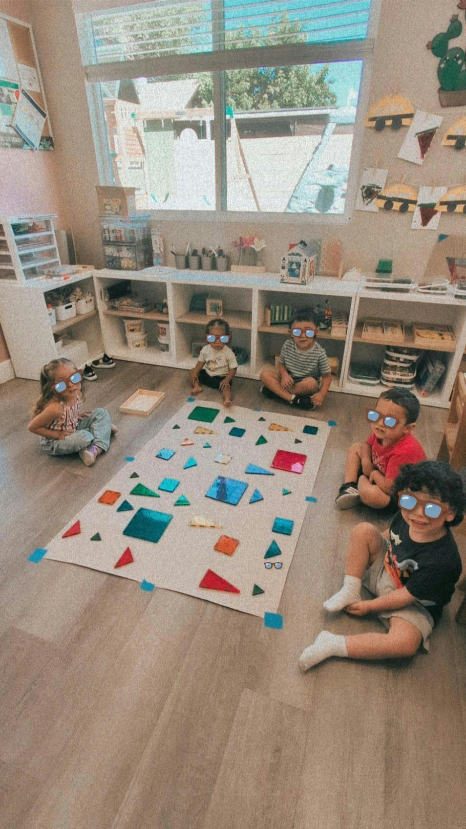 Five children sitting on the floor playing with magnetic tiles in a classroom
