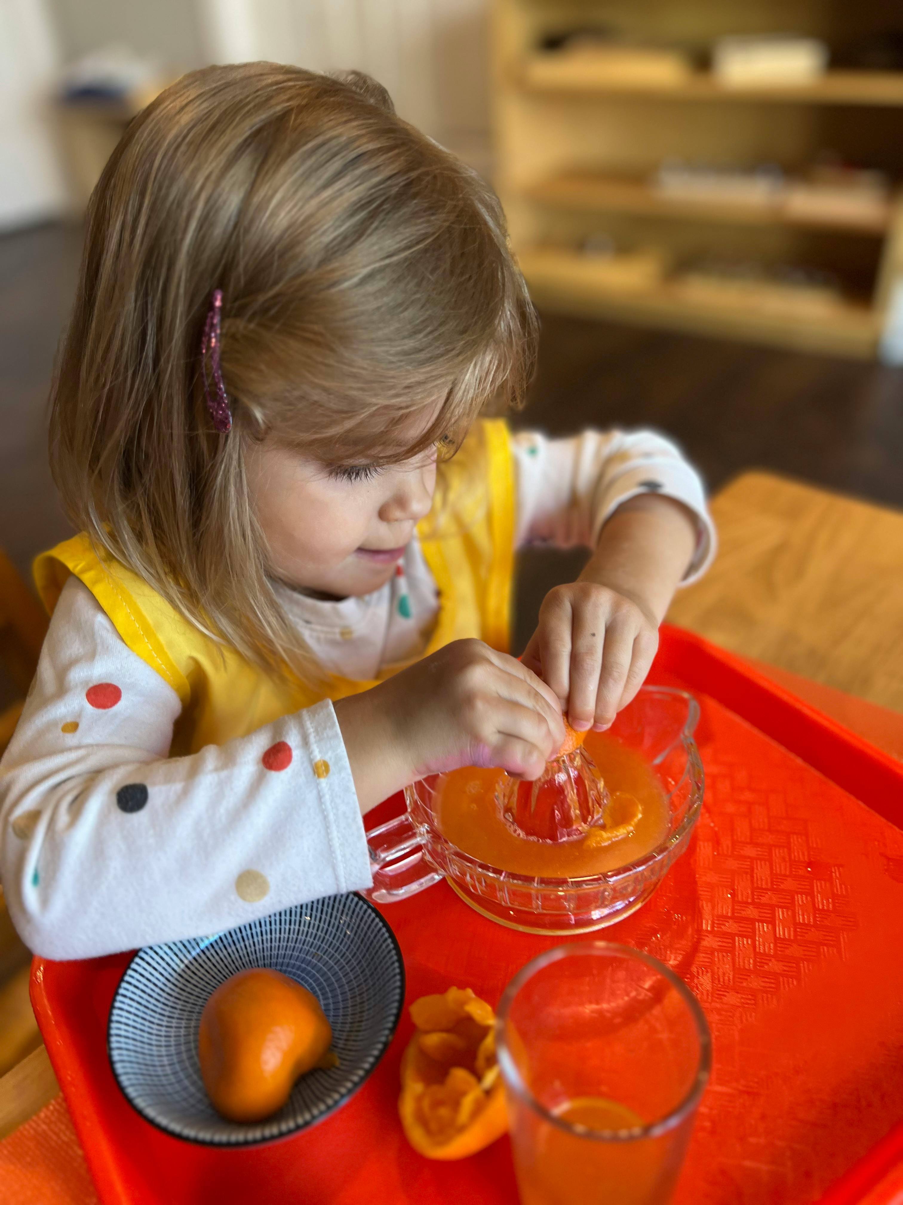 Child squeezing an orange half into a juicer on a red tray