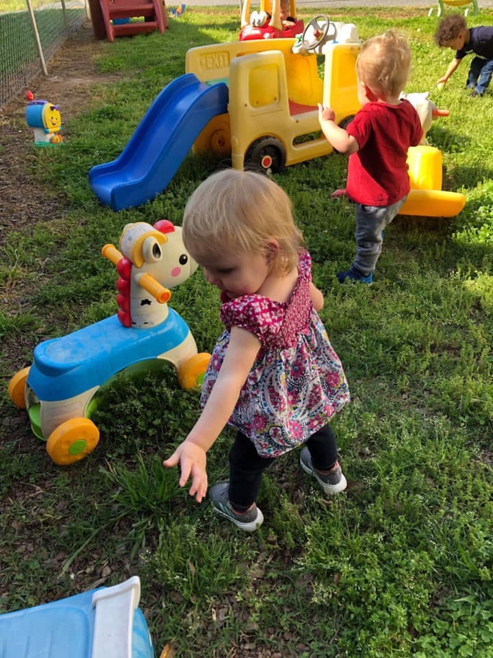 Child reaching down in grass near toys