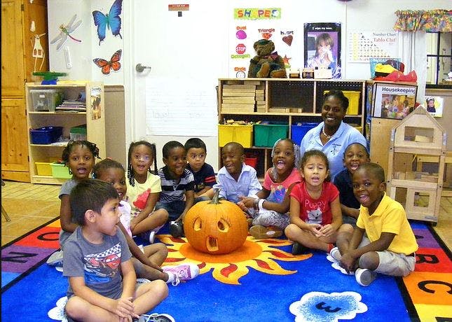 Adult and children sitting around a carved pumpkin in a classroom