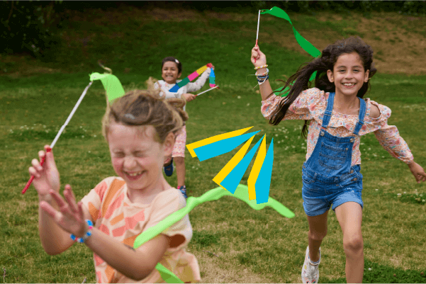 Three children running across grass, playing with colorful ribbon wands