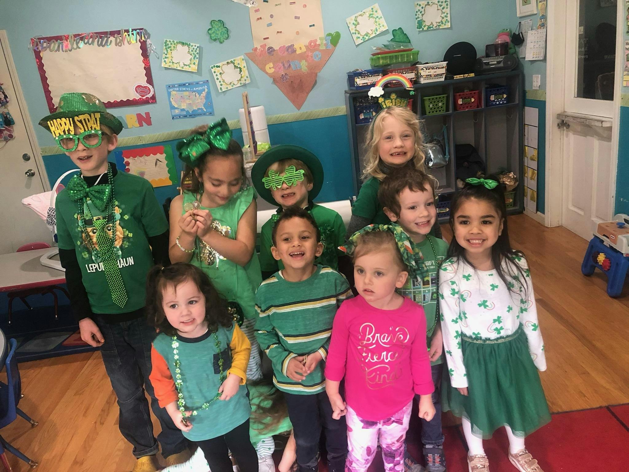 Group of children in a classroom, many wearing green clothing and accessories