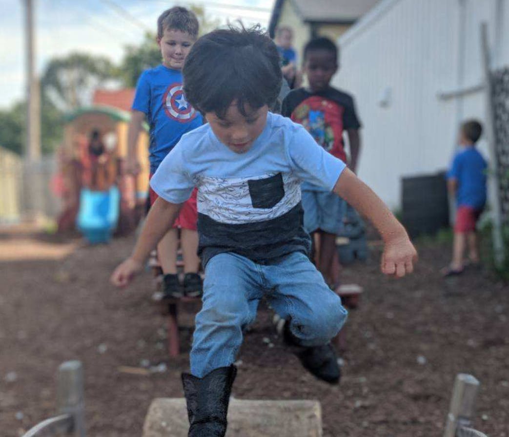 Child jumping over a log with other children in the background