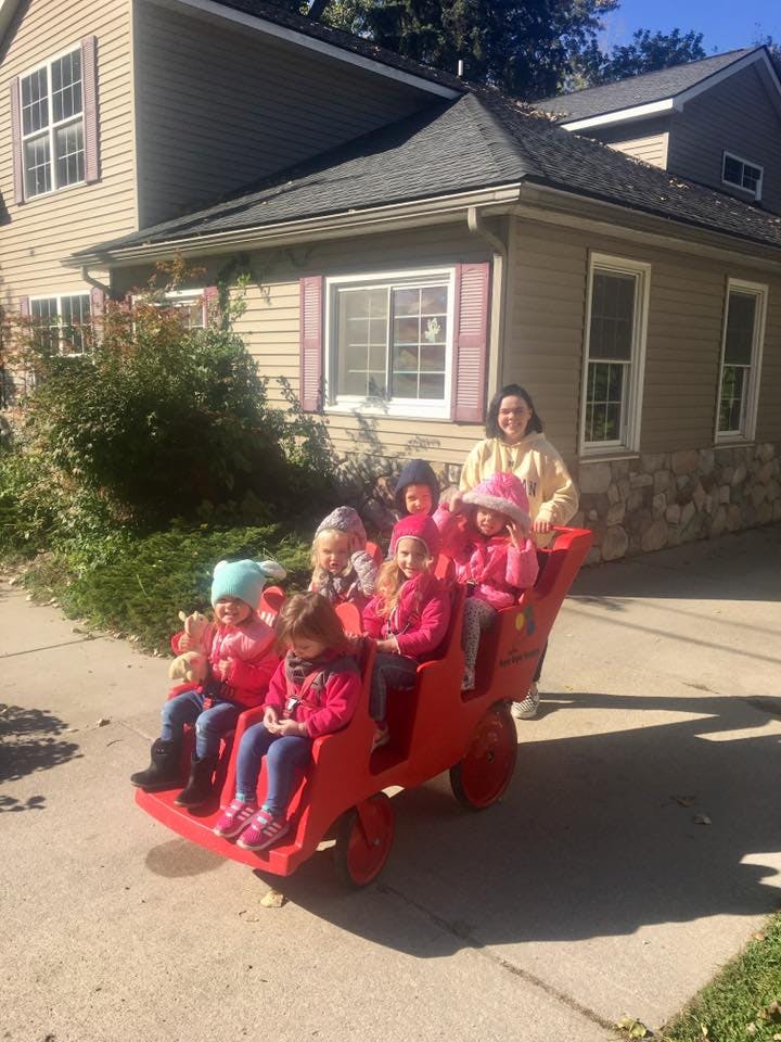 Person standing behind multiple children sitting in a red wagon