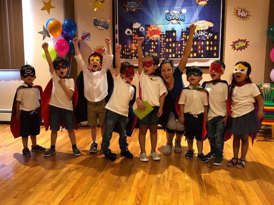 Group of children and an adult dressed as superheroes with arms raised