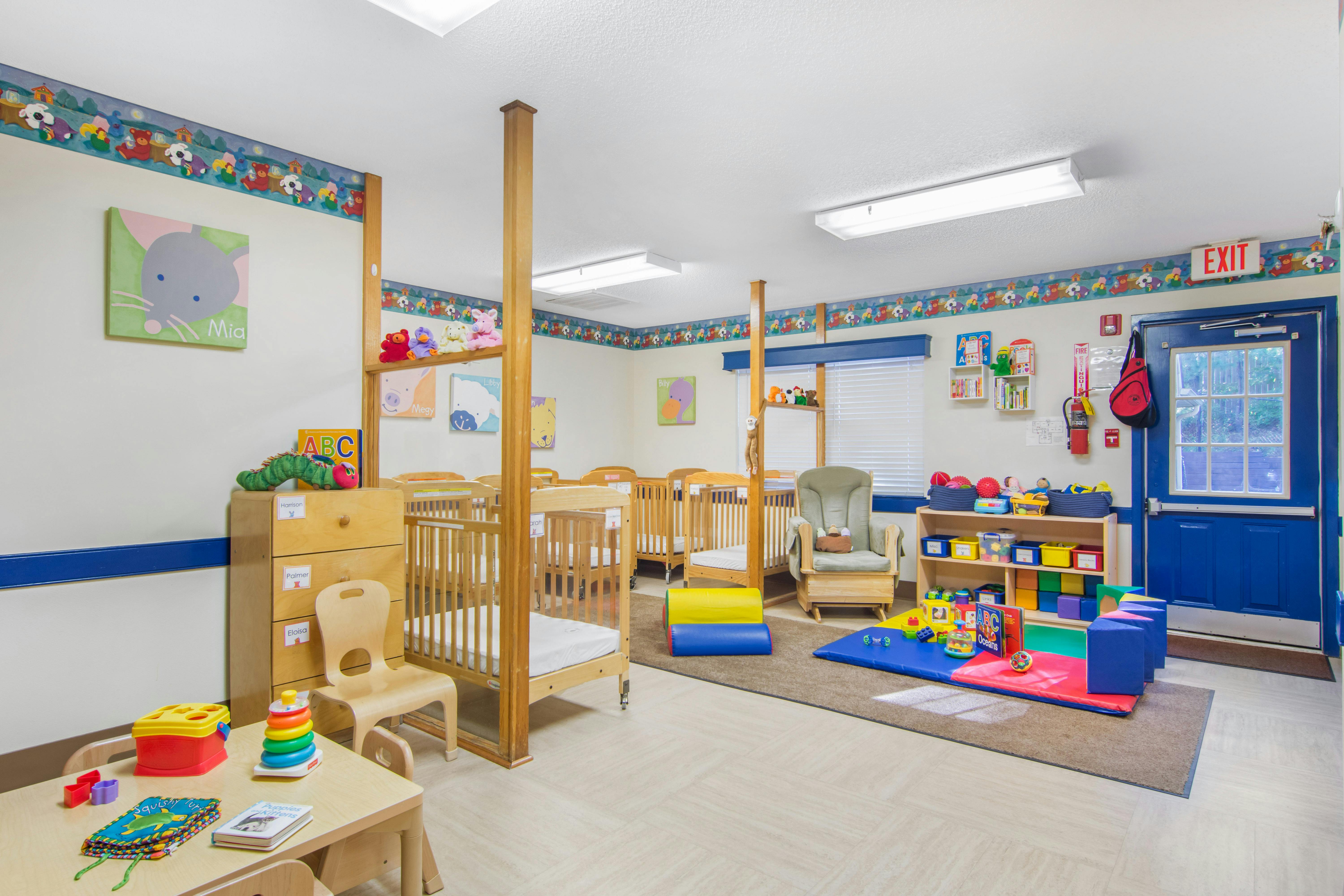 cribs in a daycare room with toys, a rocking chair, and a blue exit door